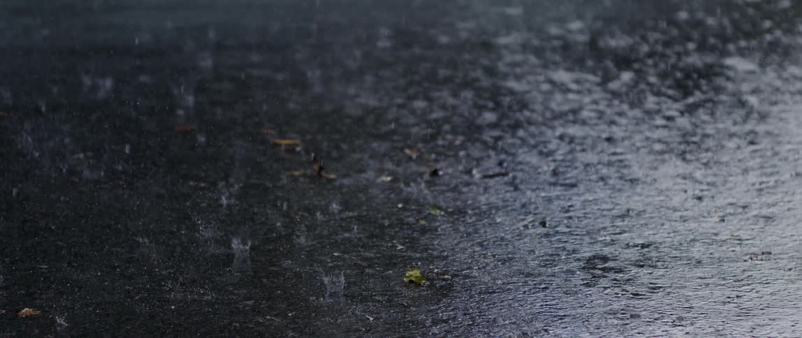 Closeup of rain falling on the asphalt at night in slow motion