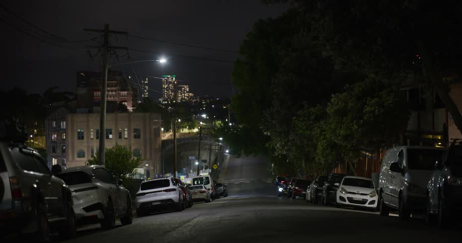 A city street at night with many parked cars
