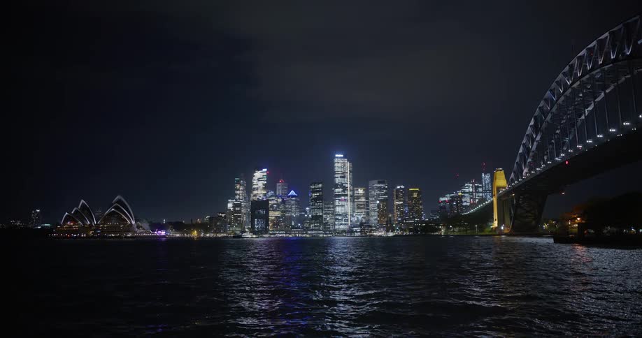View of a bridge over the sea at night with a metropolis on the horizon