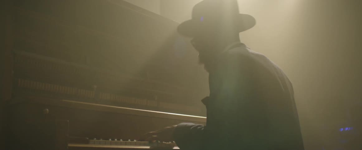 A man is energetically playing piano in a dim room