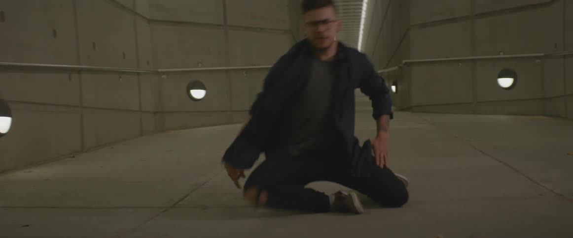 A man dances in a concrete corridor