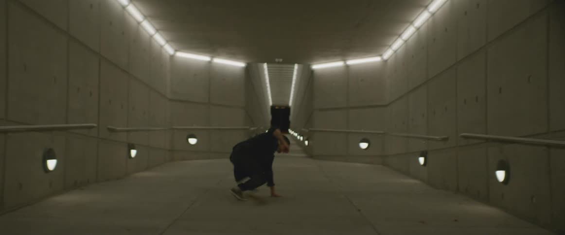 A man dances in a concrete corridor