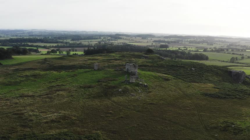 Ruins sit on hill overlooking valley containing fields and woods