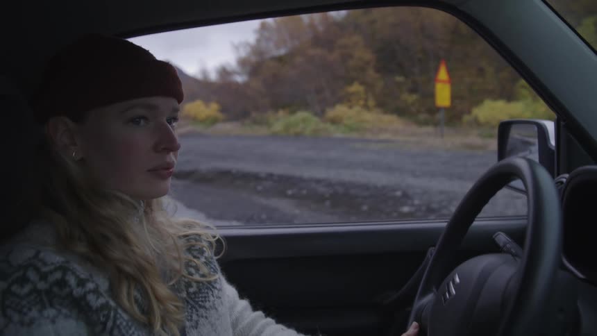 Woman drives vehicle onto road near water on a fall day