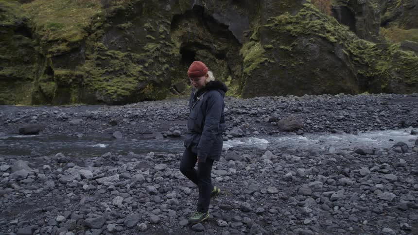 Blonde woman walking among the rocks beside a small river flowing through the mountains