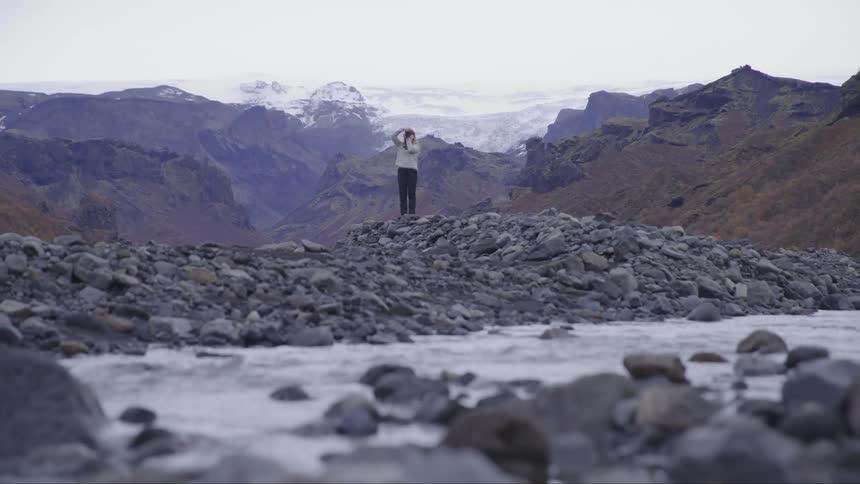 A person on the bank of a river between mountains during a cloudy day