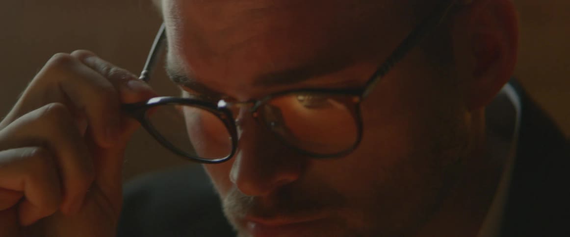 A man puts on his glasses in a dark room