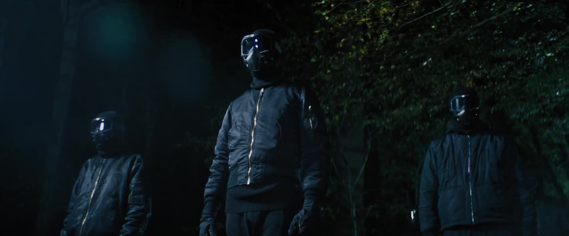 Three men wearing masks and goggles standing menacingly in the woods at night