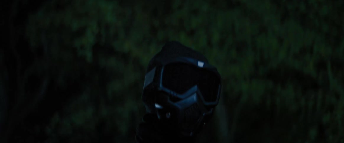 Person wearing face mask and hood walks through woods at night