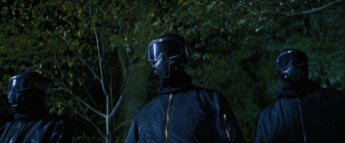People wearing dark fullface helmets with a reflective visor in a dark outdoor setting