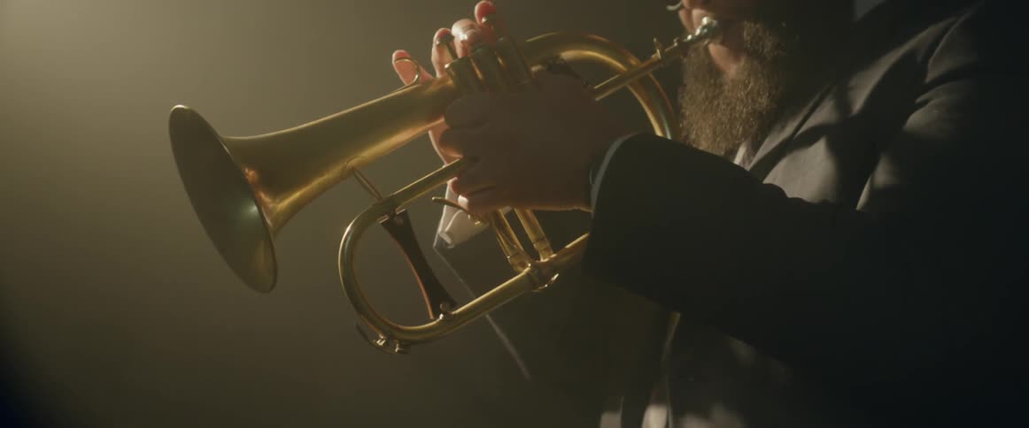A bearded man plays a trumpet