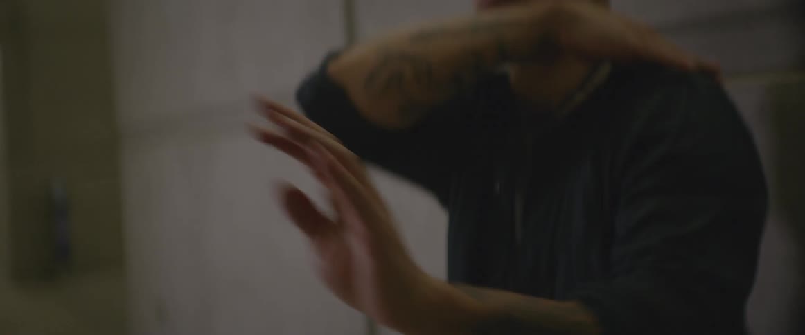 Man with tattooed arms dances in a concrete corridor