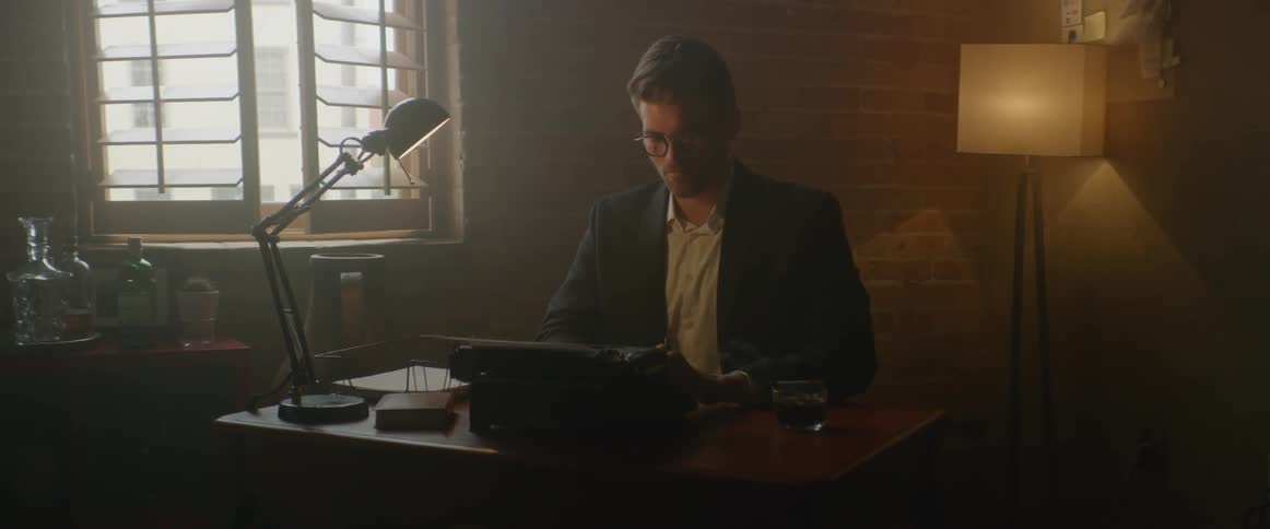 A man is typing on a typewriter in a dimly lit office