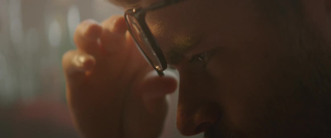 A man rubs his eyes and places his glasses back down