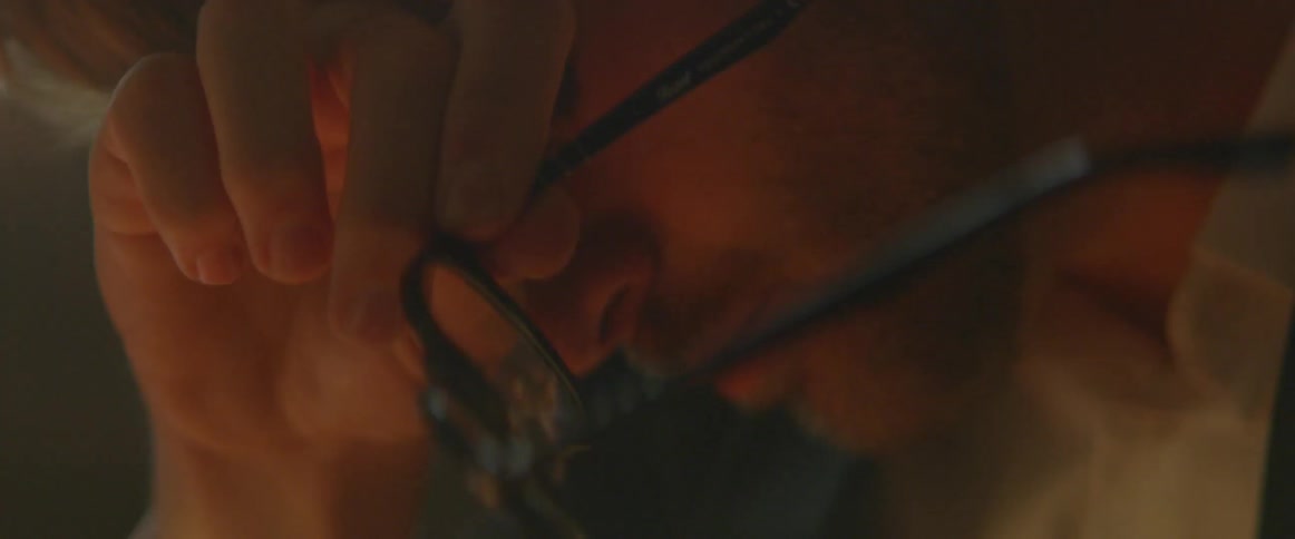 A man rubs his forehead while holding his glasses