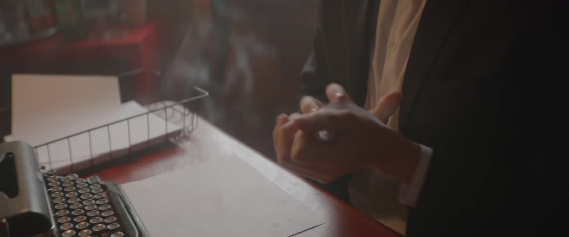 Wisps of smoke billow around a man at a desk crunching up a piece of paper