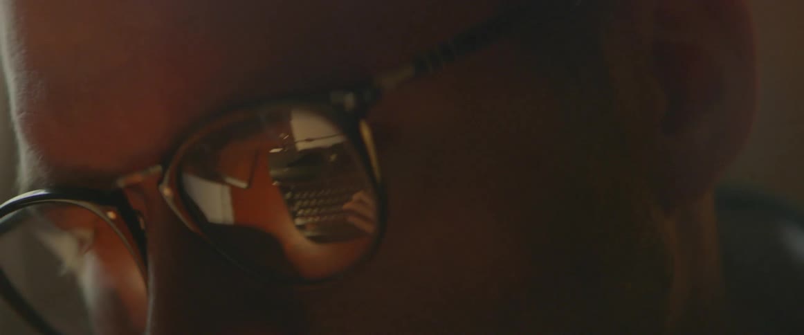 A man wearing glasses sits at a desk typing
