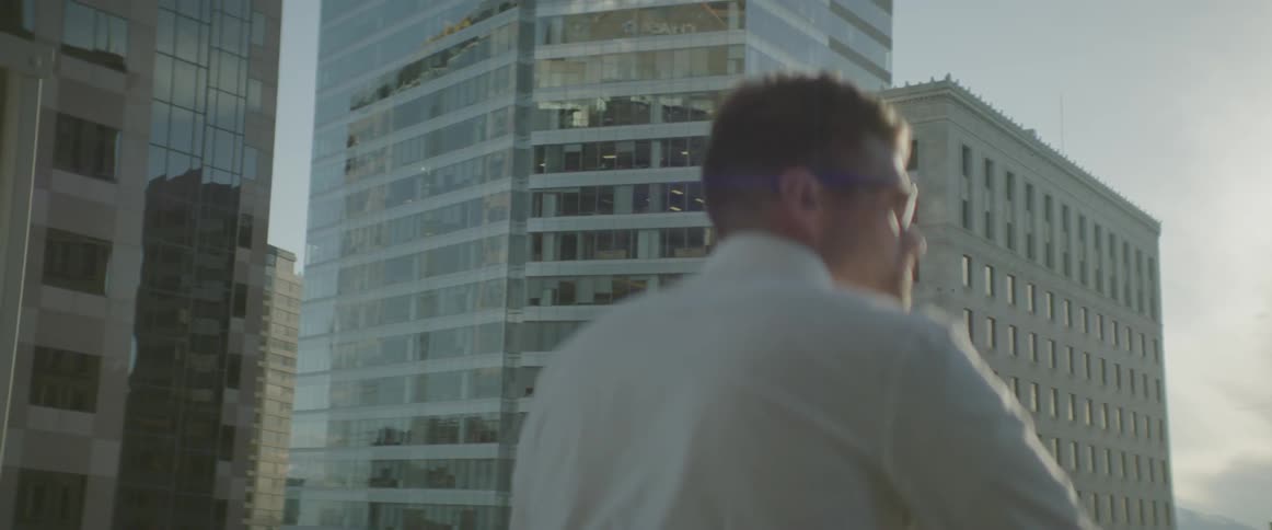 Man with glasses stands on balcony overlooking city tall buildings