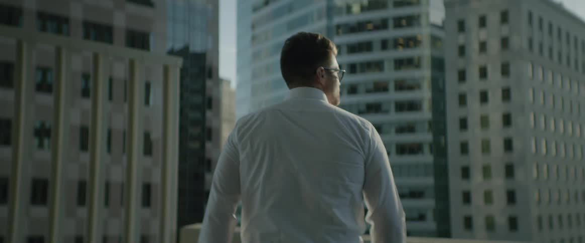 A man approaching a balcony wall and resting his hands on it as he gazes at other buildings