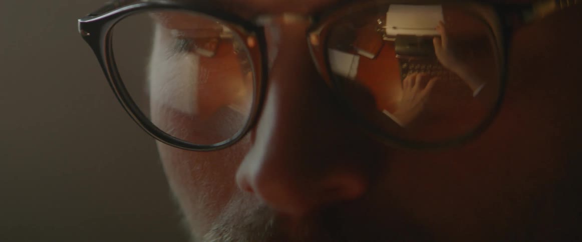A typewriter is seen in a man's glasses as he works