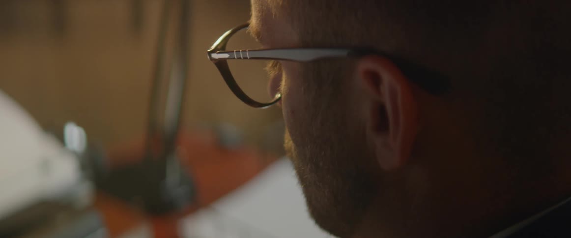 A man wearing glasses sits at a desk