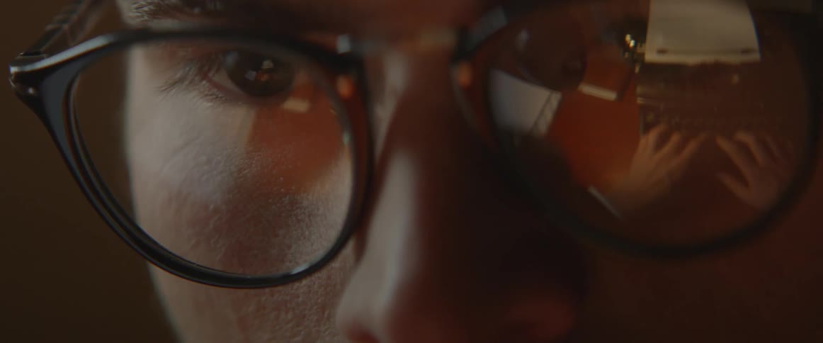 A man is wearing glasses reflecting a typewriter that he is using