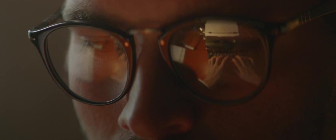 The reflection of a man using a typewriter is seen in his glasses