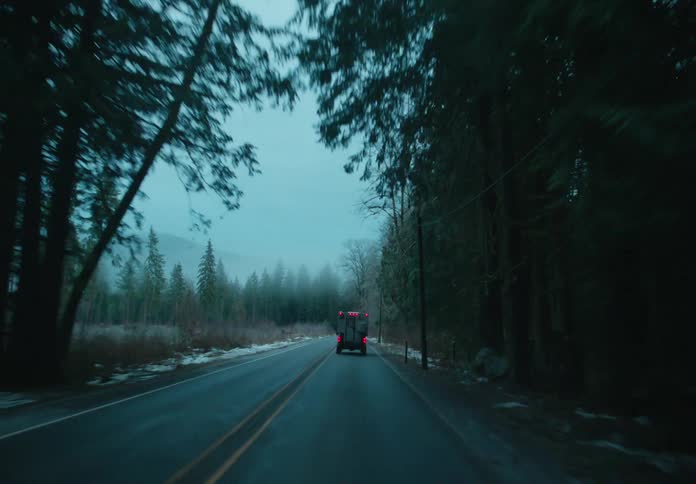 A truck travels on a road through the forest with snow on the roadside