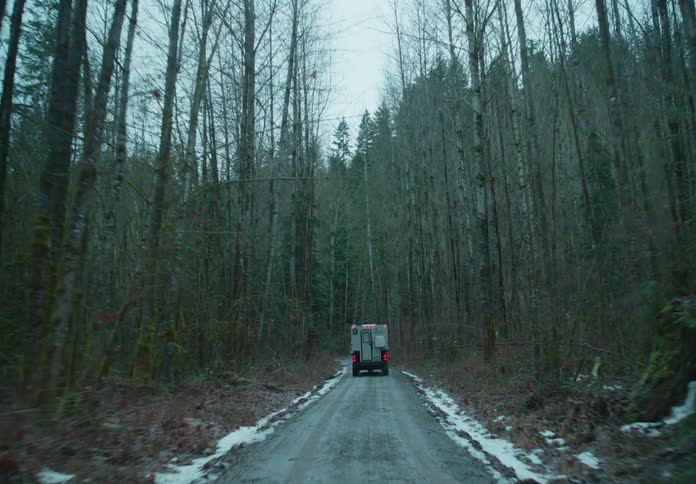 Van with a camper driving on a dirt road through a forest on a cloudy day