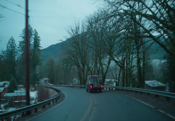 A pickup truck with a camper shell is driving on a road through a small rural town