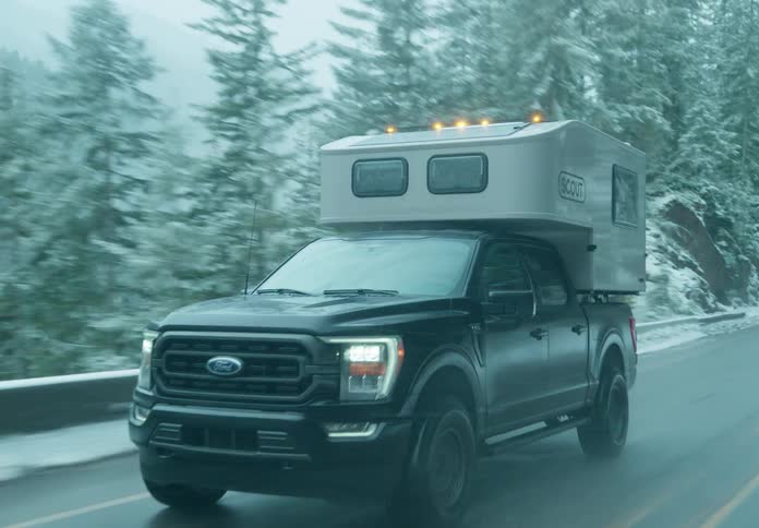 A pickup truck with a camper shell is driving on a road in the mountains