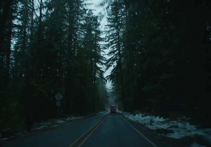 View of a highway with a small truck in motion through a winter forest