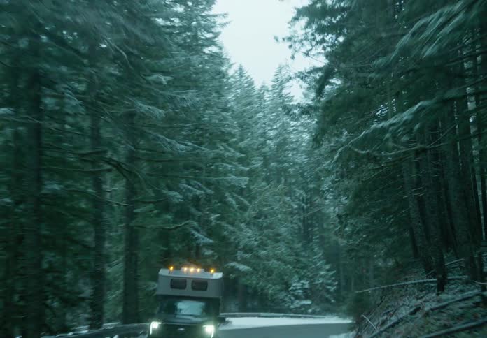 A large car driving on an asphalt road and on the sides there are trees with snow