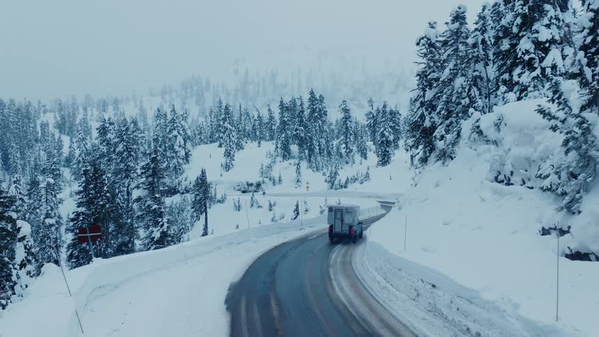 A pickup truck with a camper shell is driving on a snowy road in the mountains