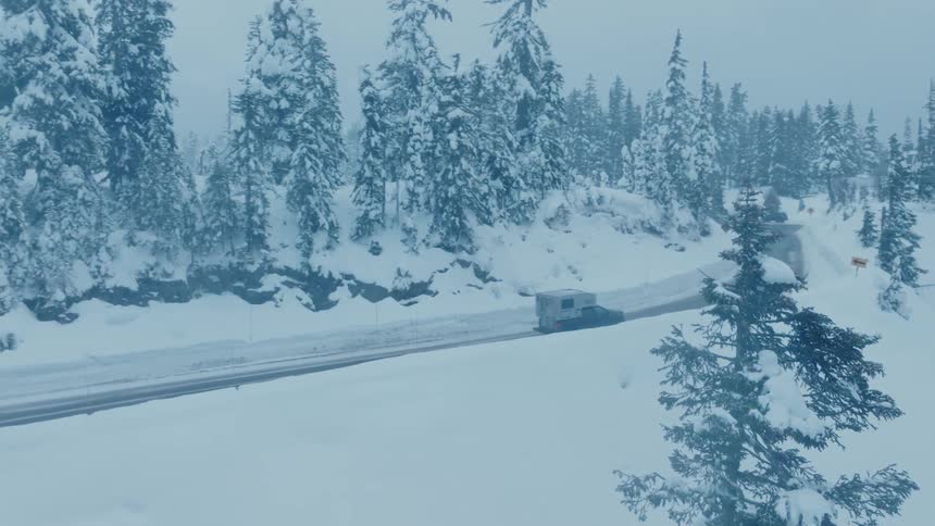 A vehicle drives down the road by the snow covered forest