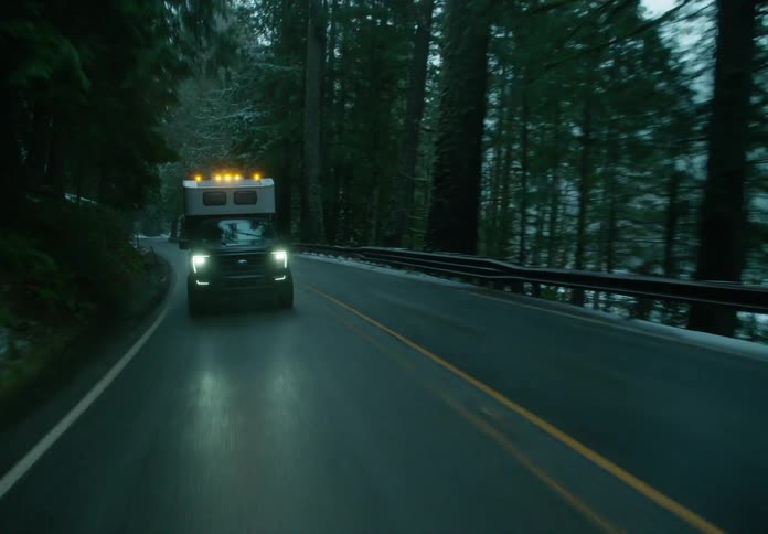 Pickup truck with camper shell drives along highway through snowy conifer forest bordering river