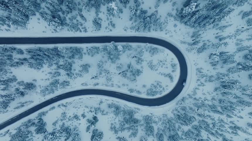 A car driving on a winding road through a snow covered forest