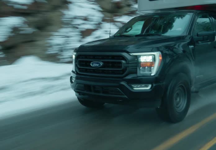 A pickup truck driving on a snowy road with trees on the sides