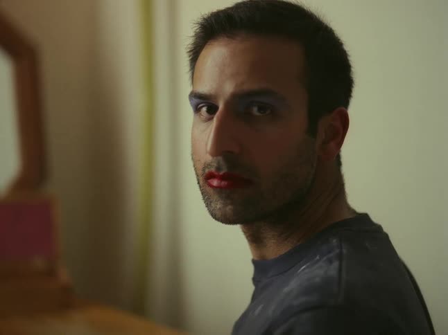 Close up of the face of a man wearing makeup looking at the mirror