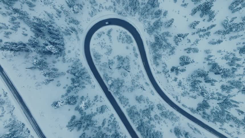 A car driving on a street with a large curve in an area with lots of snow and trees