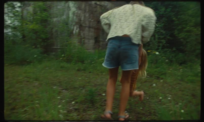 A girl is standing on the edge of the woods swinging her little sister around by the hands