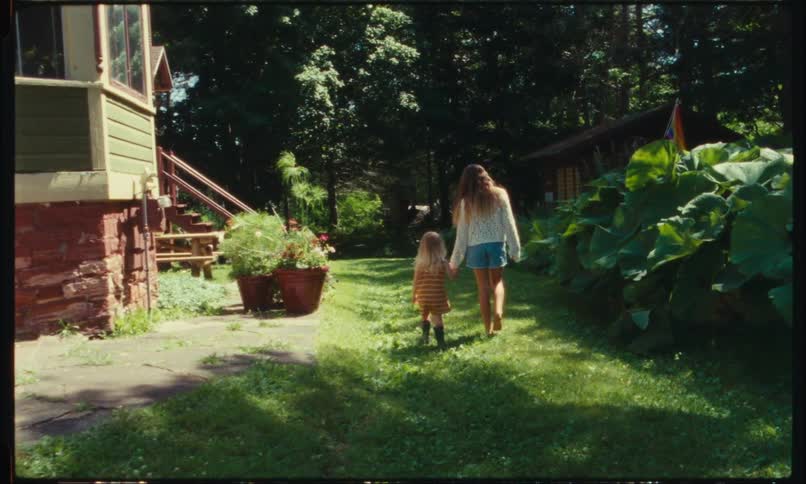 Mother walking hand in hand with her daughter in the backyard on the grass at home