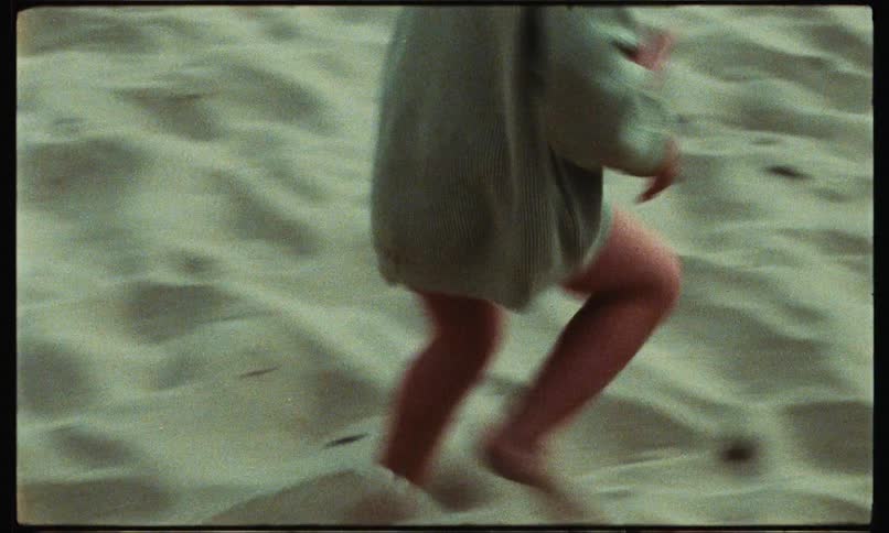 A small female toddler is running on a sandy beach