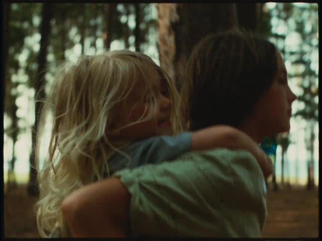 Girl is carrying her little sister on their back in a forest
