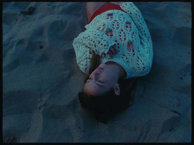 Girl wearing a white sweater and red swimsuit resting in the sand beach