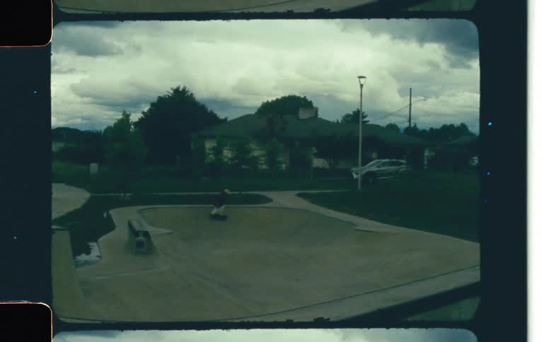 Skateboarder rides skateboard through skate bowl in park across the street from houses on a cloudy day