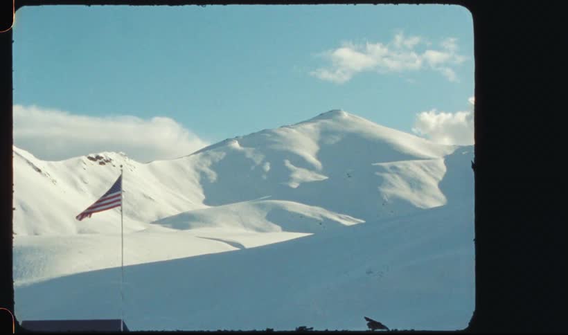 A snow white mountain and a country flag moving in the wind