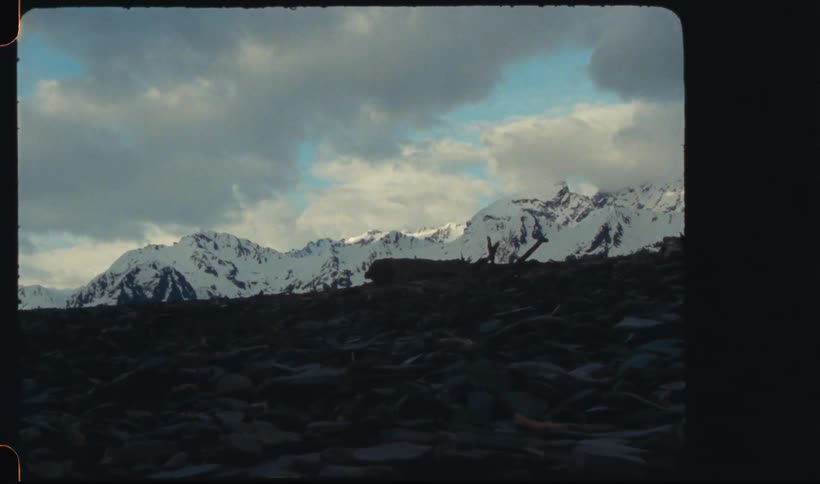 Landscape of black rocks with mountain ranges covered in snow on a day with a sky filled with heavy clouds