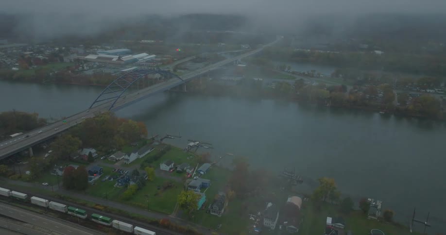 Train passes bridge crossing river near houses on a foggy fall day