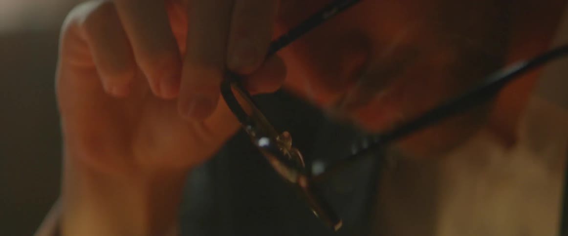 A wisp of smoke rises up toward a man who is holding a pair of glasses